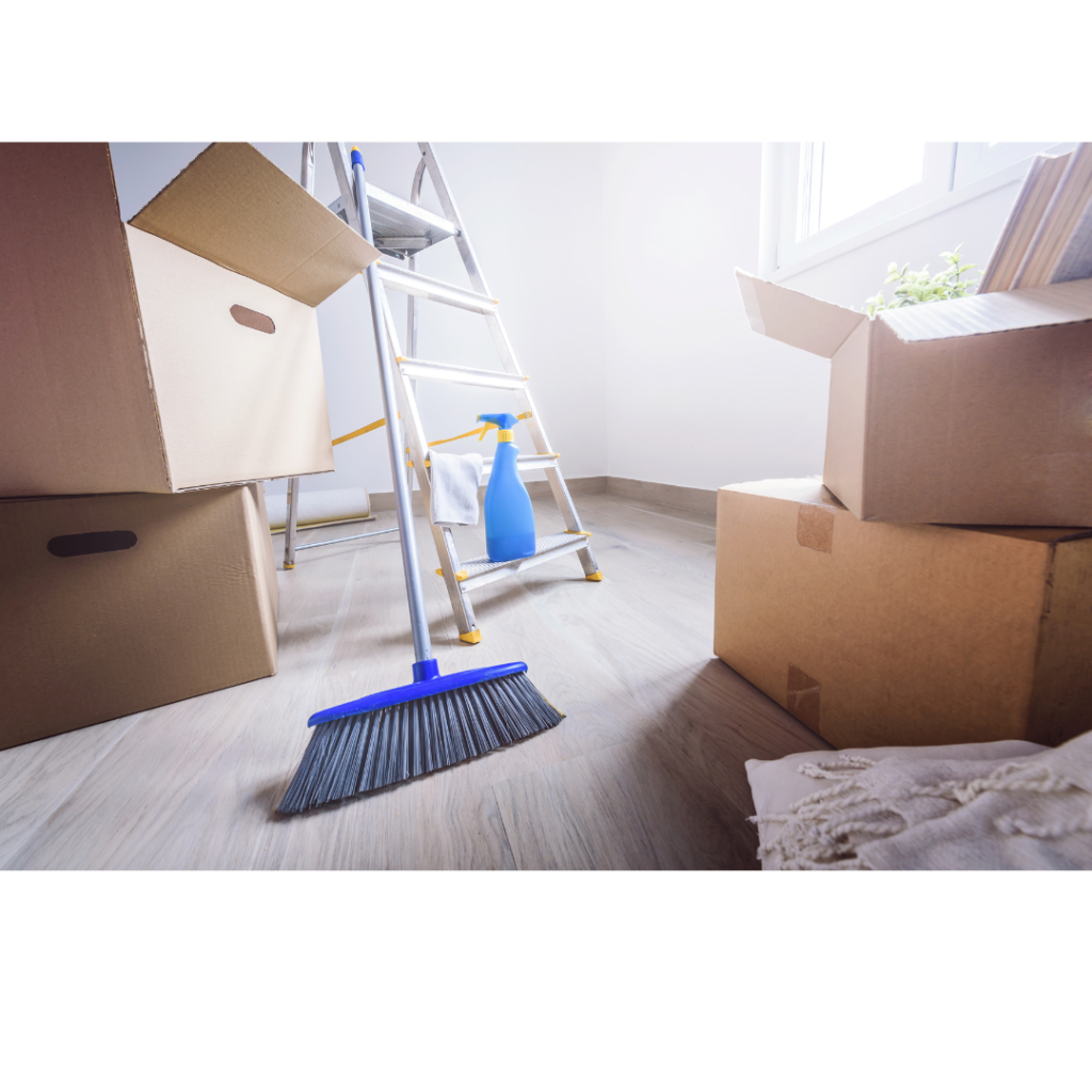 A broom and cleaning tools are seen in a box full of moving boxes.