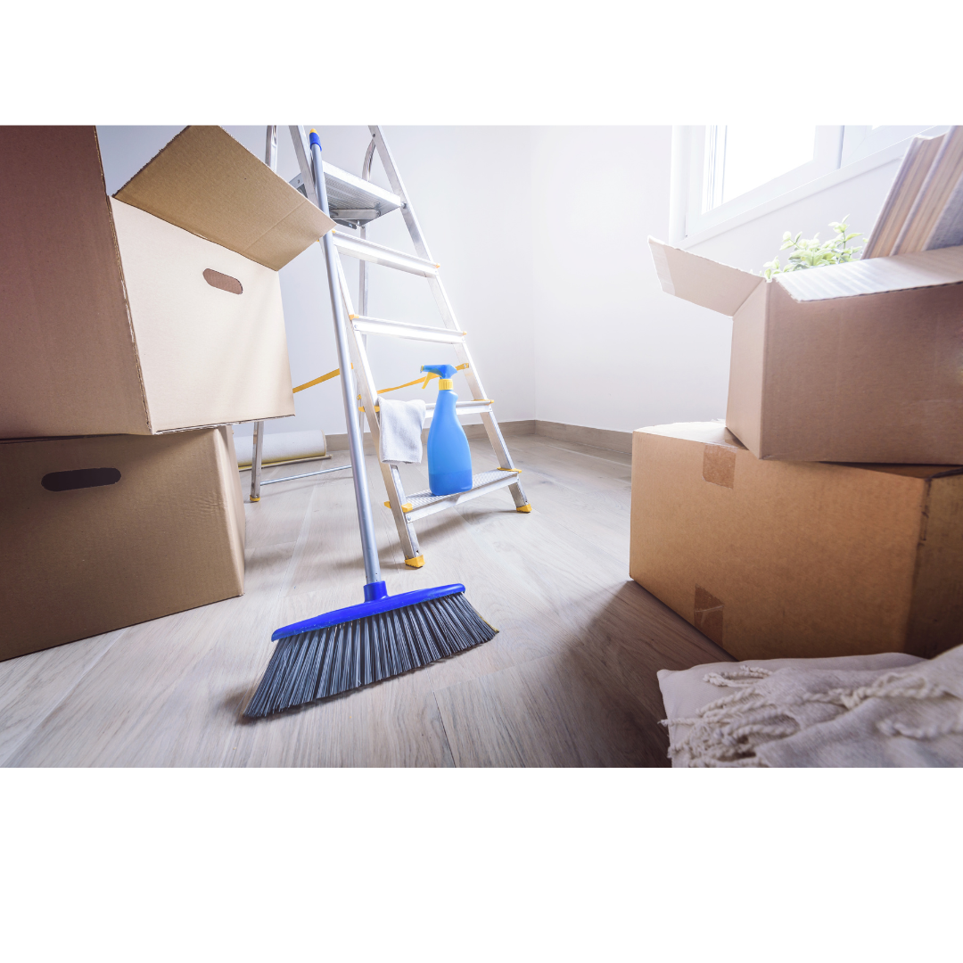 A broom and cleaning tools are seen in a box full of moving boxes.