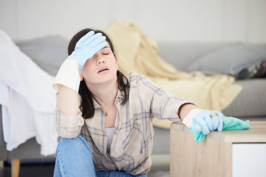Exhausted woman wears cleaning gloves as she cleans a messy house.